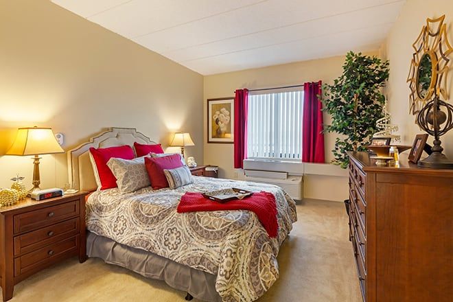 A cozy bedroom with elegant decor, featuring a comfortable bed adorned with red accents and warm lighting.