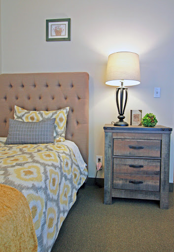 A cozy bedroom featuring a stylish tufted headboard, patterned bedding, a rustic nightstand with a lamp, and greenery for a touch of freshness.