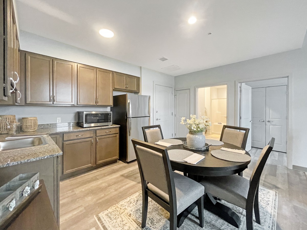 A modern kitchen and dining area featuring a round table set for four, with wooden cabinets and stainless steel appliances.
