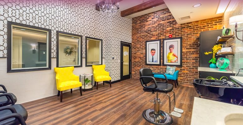 A modern salon interior featuring bright yellow chairs, a brick accent wall, and stylish decor.