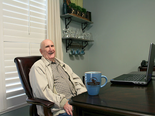 An elderly man sitting comfortably at a table with a cup, enjoying his time indoors.