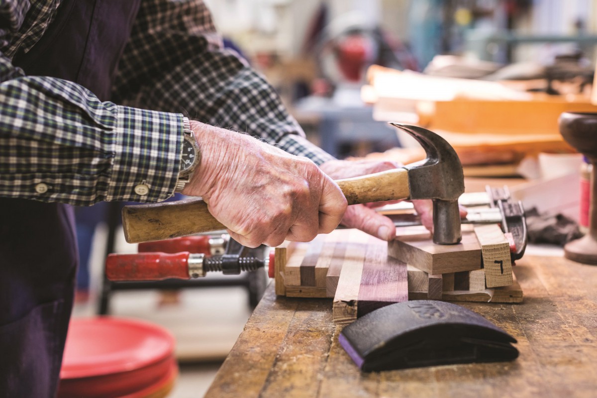 A carpenter using a hammer in a workshop to work on a piece of wood.