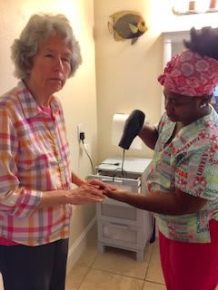 A caregiver assisting an elderly woman with hand care, using a handheld device.