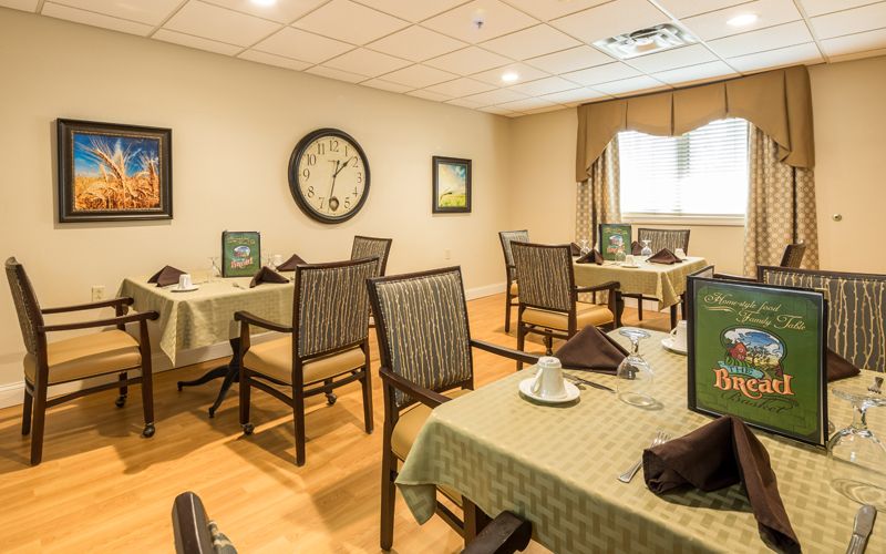 Cozy dining room with neatly arranged tables and chairs, featuring a wall clock and window.