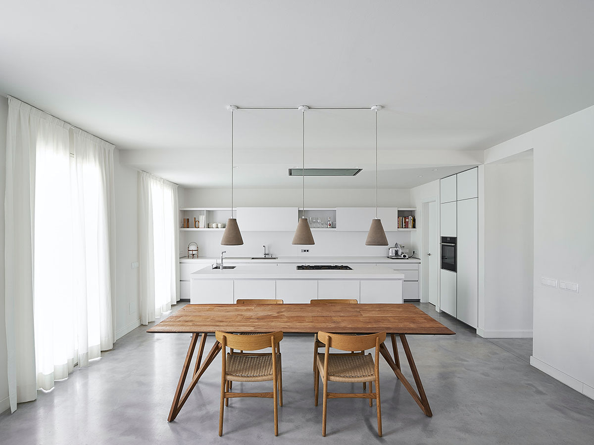 A minimalist kitchen with a wooden dining table and modern pendant lights.