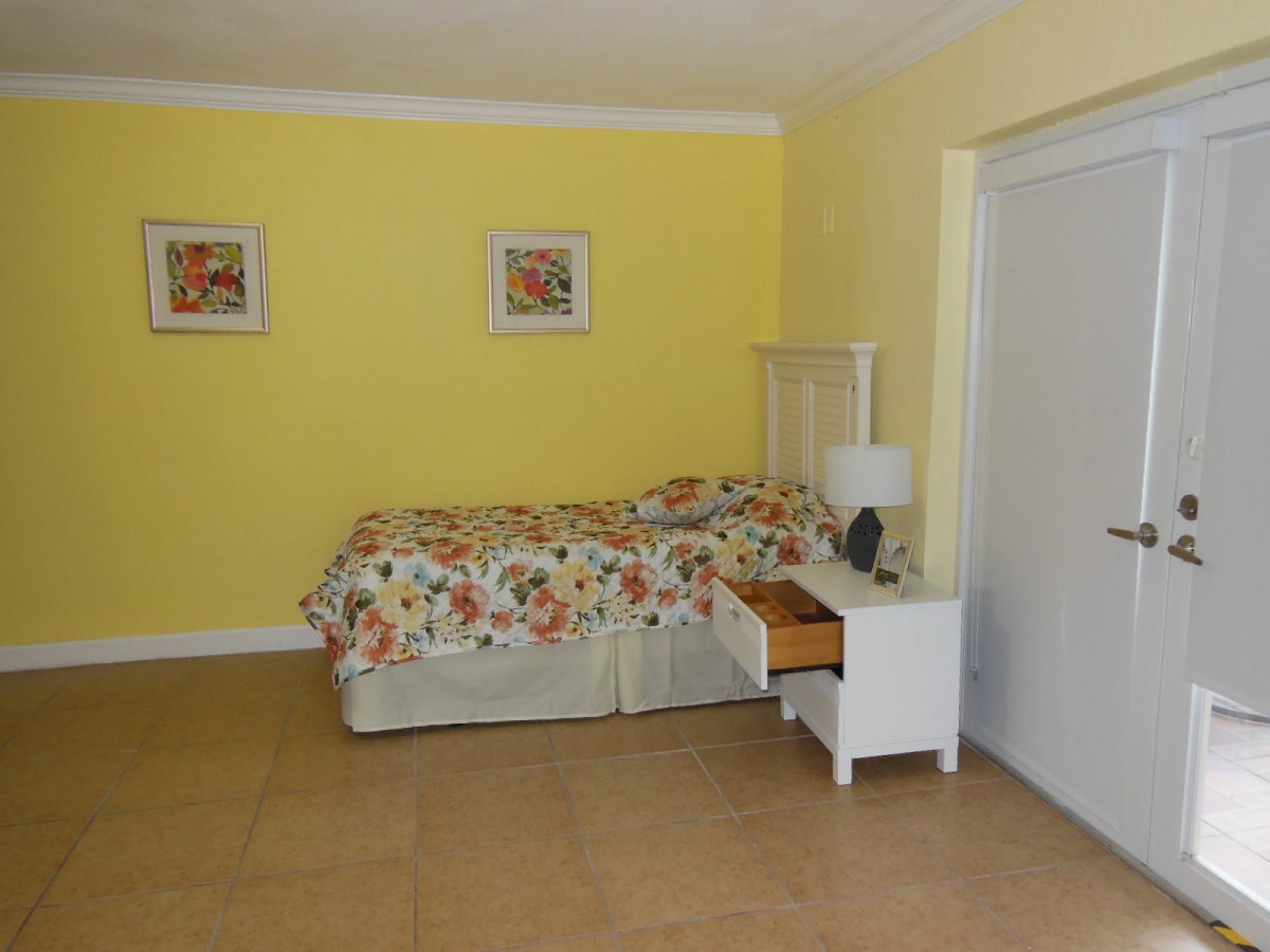 A cozy bedroom with yellow walls, featuring a single bed adorned with floral bedding and a nightstand with a lamp.
