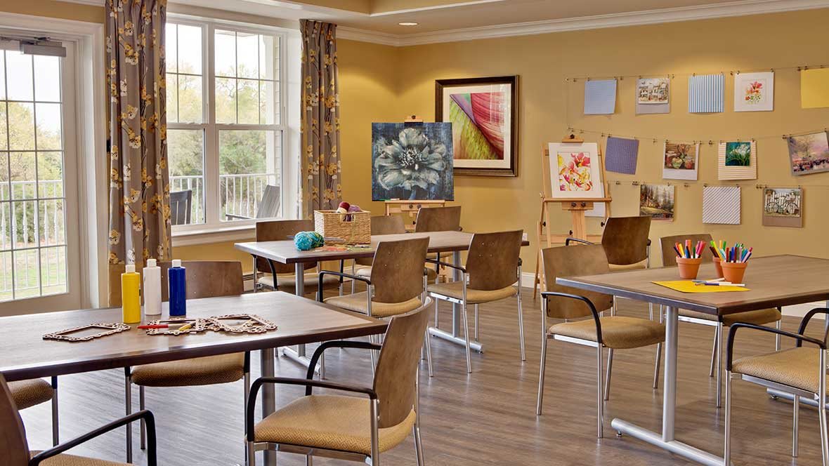 A brightly lit art studio with tables, chairs, and various paintings on easels.