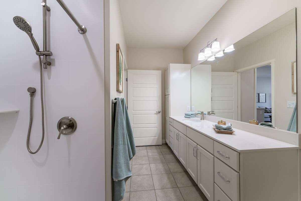 A modern bathroom with dual sinks, white cabinetry, and bright overhead lighting.