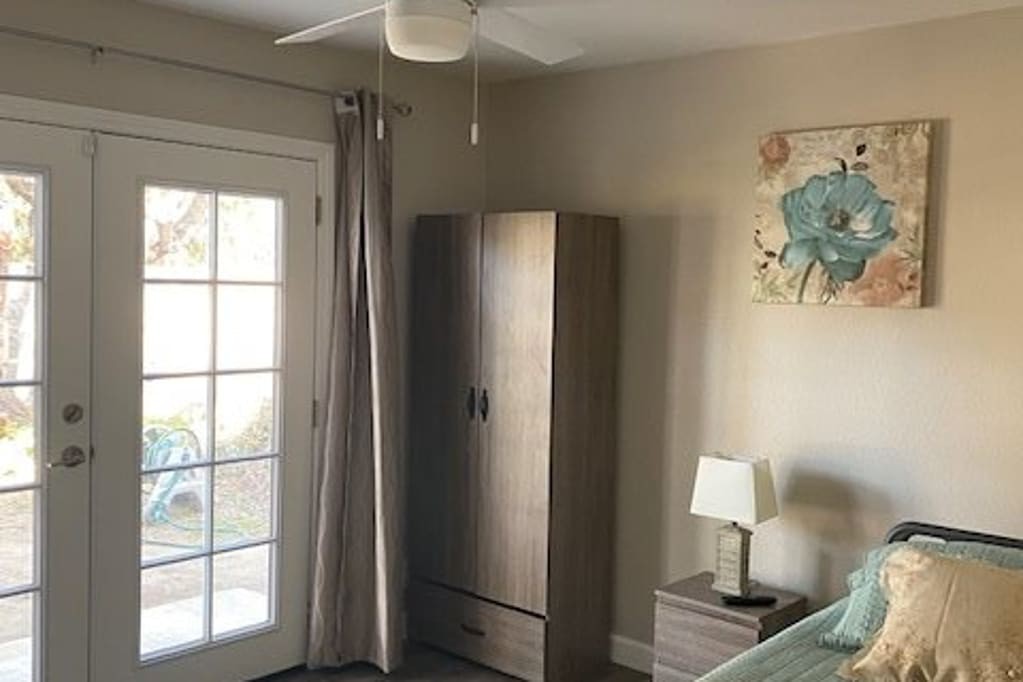 A cozy bedroom with a wardrobe, lamp, and ceiling fan next to French doors.