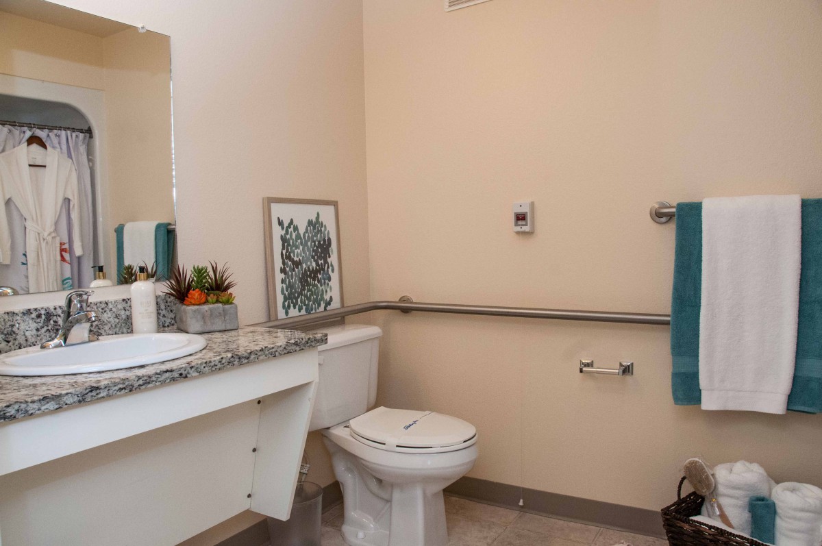 A clean and accessible bathroom with a toilet, sink, mirror, and handrails.