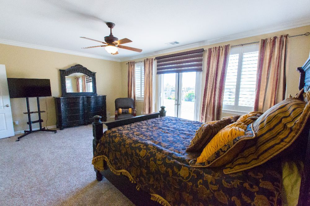 A well-decorated bedroom featuring a dark wood bed and dresser, with large windows and elegant curtains.
