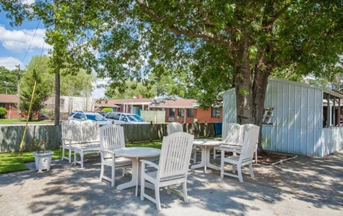 An outdoor patio area with white chairs and tables under the shade of a large tree.