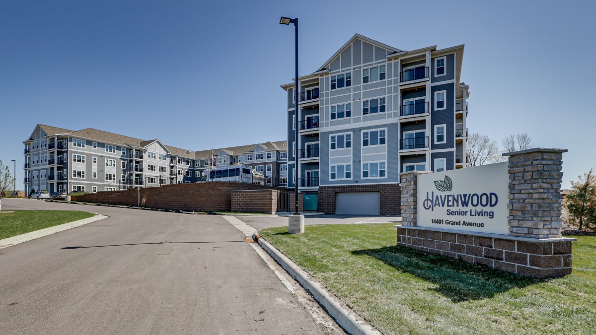 A modern apartment complex with multiple stories, featuring a sign at the entrance.