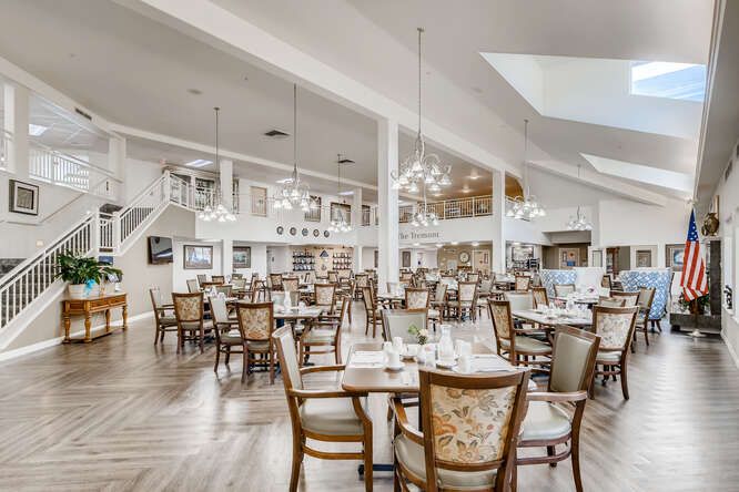 A spacious and elegant dining area with numerous tables and chairs, illuminated by chandeliers.