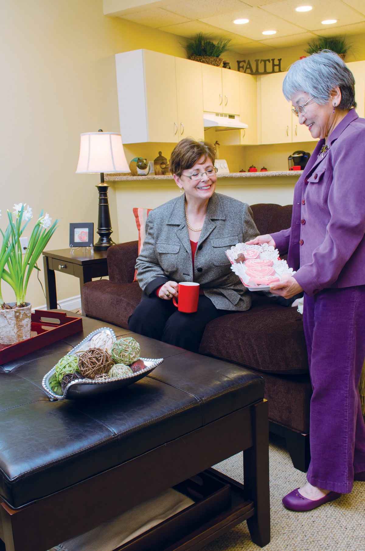 Two women having a conversation in a living room, with one holding a gift while the other holds a coffee mug.