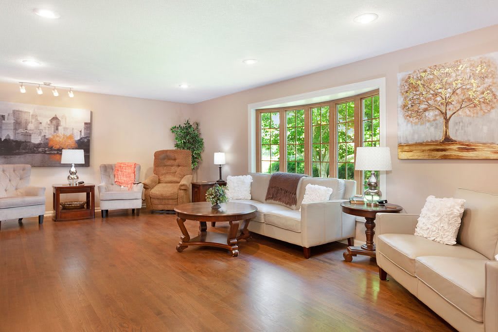 A cozy and bright living room with large windows, comfortable furniture, and wooden flooring.