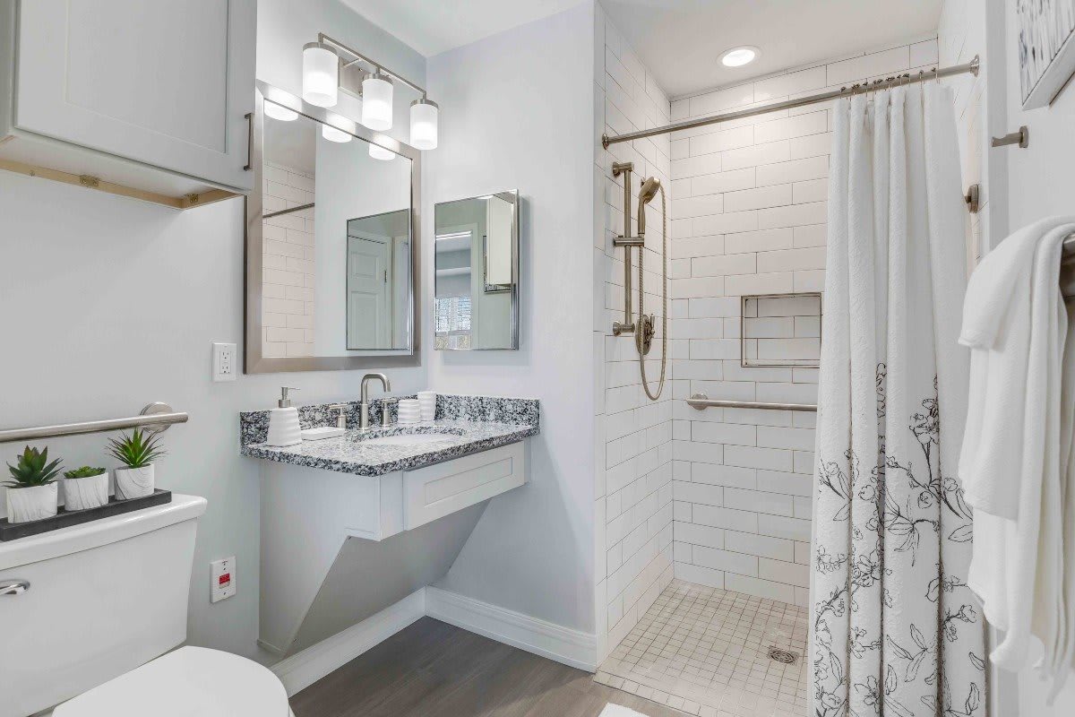 A modern bathroom interior featuring a shower with white tiles, a sink with a mirror above, and elegant lighting.