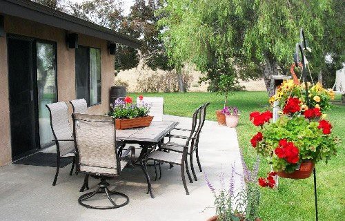 A well-maintained patio with outdoor furniture surrounded by a lush garden and colorful flowers.