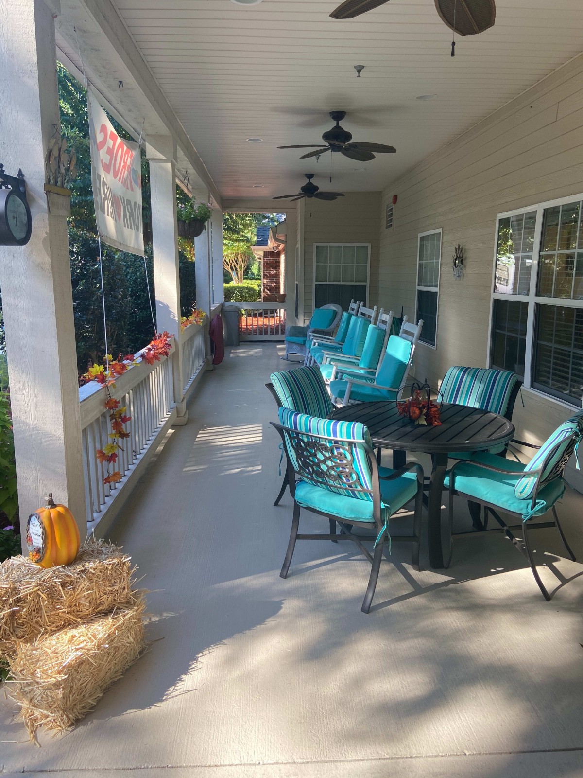 A cozy outdoor patio decorated with a fall theme, featuring a table and chairs surrounded by seasonal decorations like pumpkins and hay bales.