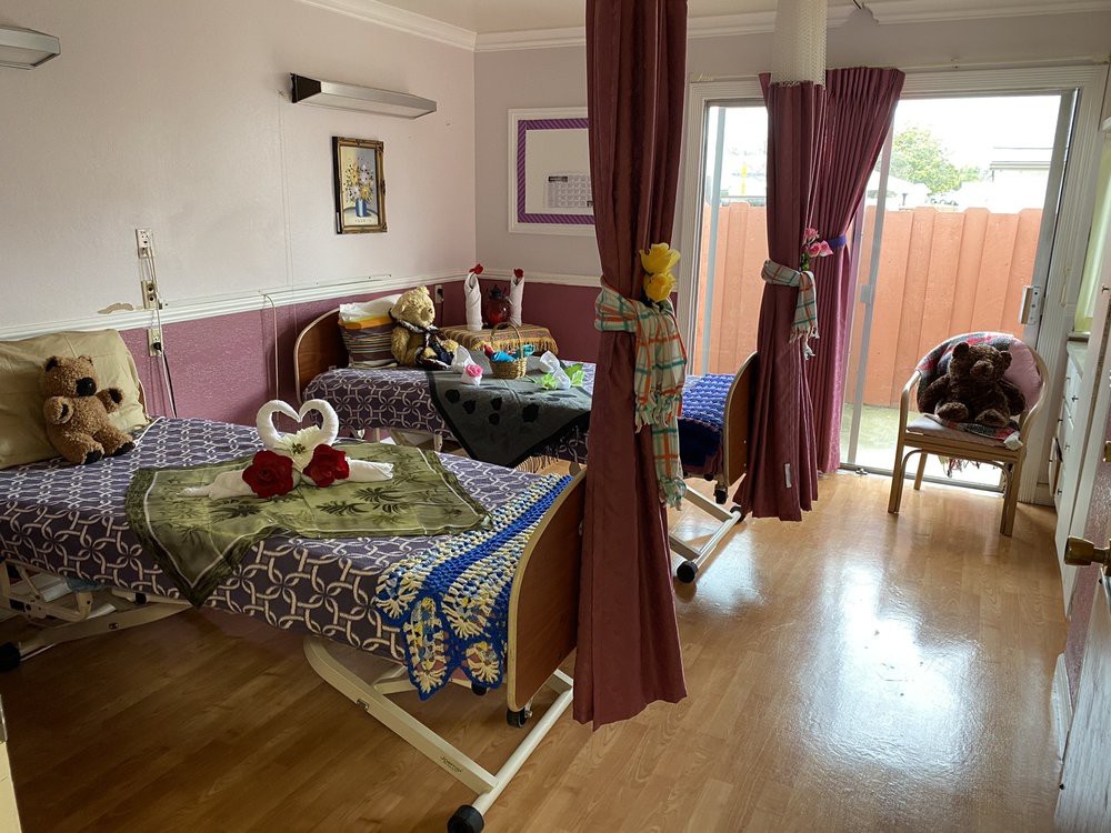 A shared hospital room with two patient beds, separated by curtains, and decorated with floral arrangements.