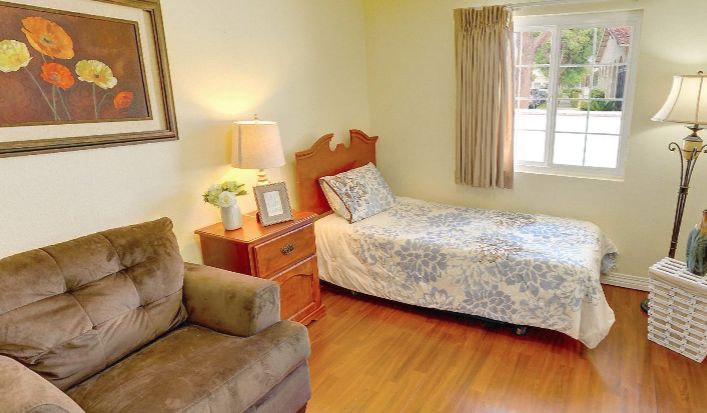 A cozy bedroom with a single bed, a nightstand with a lamp, and a comfortable chair by the window.