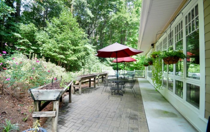 A scenic outdoor patio with tables and red umbrellas, surrounded by lush greenery.