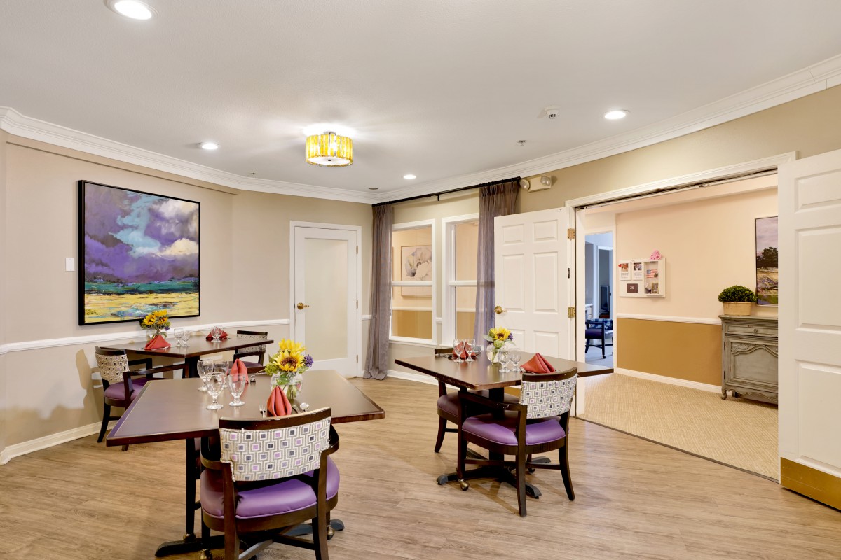 A cozy and well-decorated dining area with tables and chairs, featuring a colorful painting on the wall.