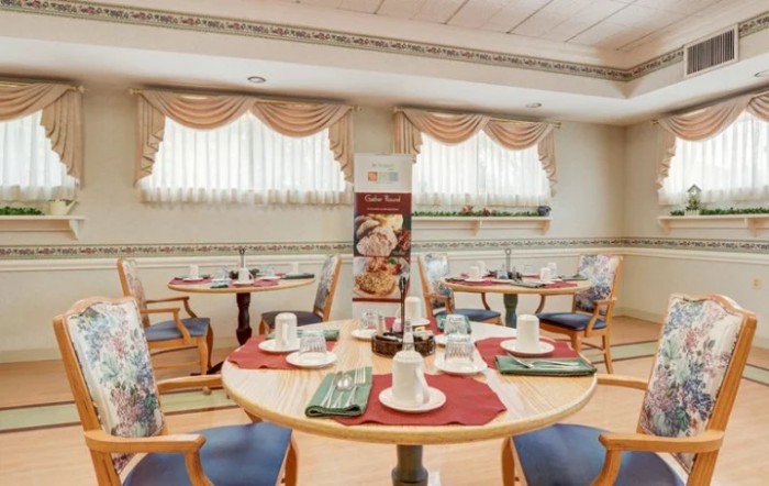 A neatly arranged dining room with several tables set for a meal, featuring elegant place settings and decorative curtains.