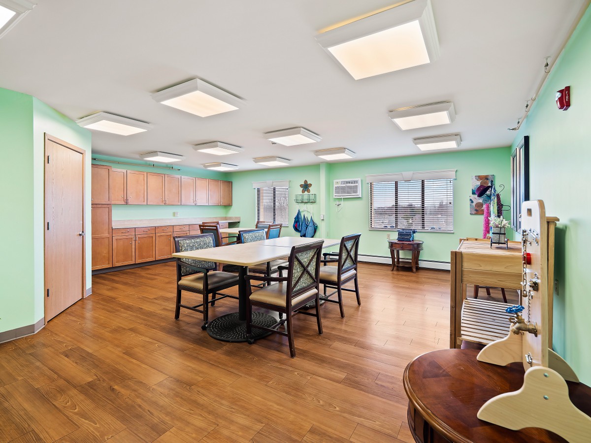 A spacious office meeting room with wooden flooring and green walls, featuring tables and chairs arranged for group discussions.