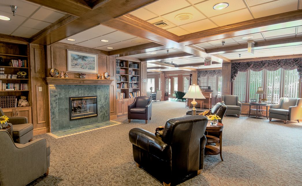 A cozy living room with wood paneling, featuring a fireplace, armchairs, and bookshelves.