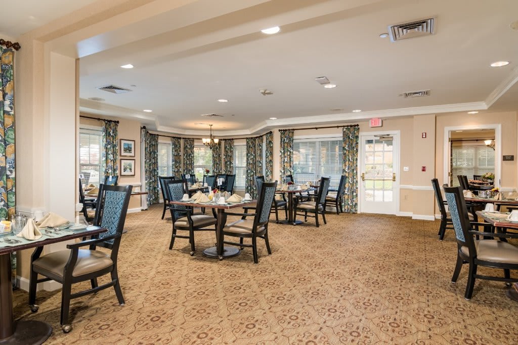 A spacious dining room with several tables and chairs, featuring elegant lighting and large windows.