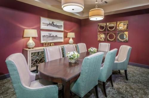 An elegant dining room with a long wooden table surrounded by upholstered chairs, adorned with wall art and soft lighting.