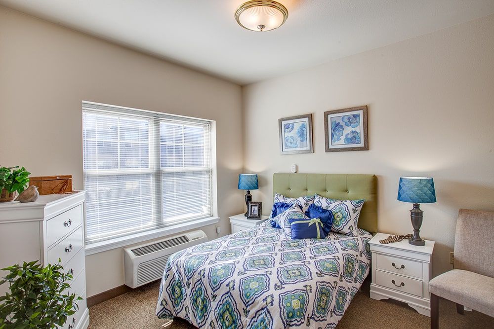 A cozy bedroom with a patterned bedspread, blue lamps, and framed artwork on the walls.