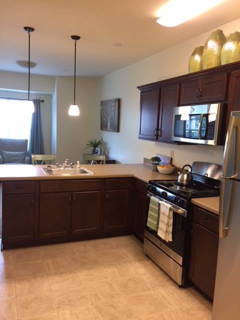 A modern kitchen with wooden cabinets, stainless steel appliances, and pendant lighting over the countertops.