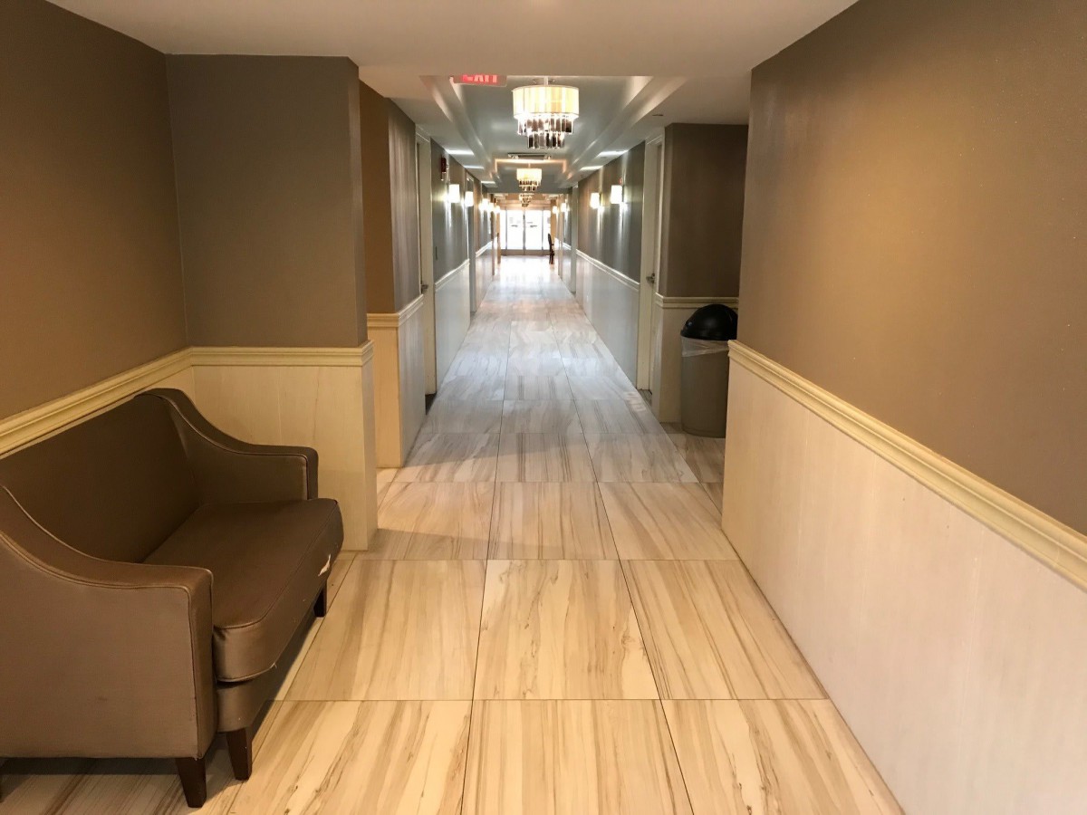 A long, well-lit hallway with tile flooring and a chair placed near the wall.