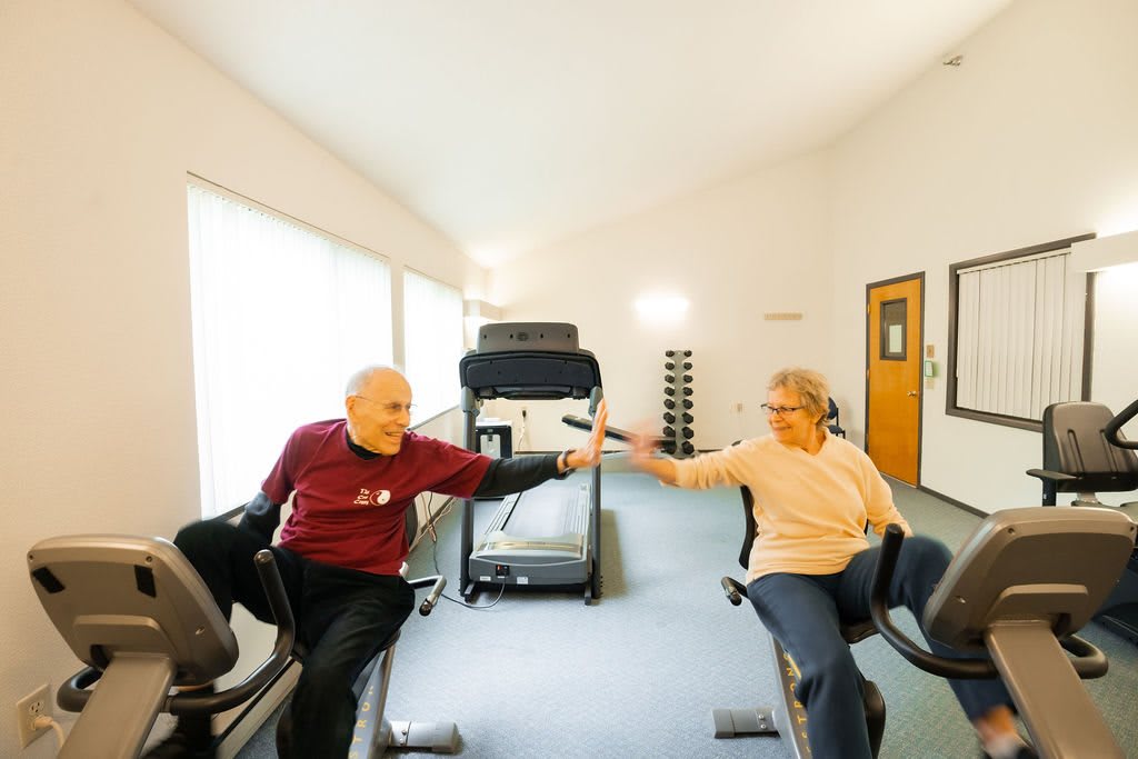 An elderly couple enjoying a workout session on exercise bikes at the gym.
