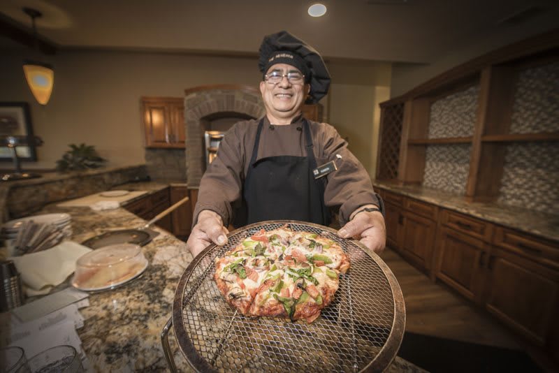 A chef proudly presenting a freshly made pizza in a kitchen setting.