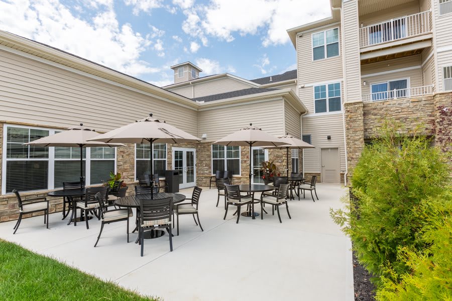 A sunny outdoor patio area with tables, chairs, and umbrellas at a residential complex.