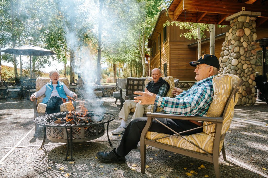 A group of people enjoying a conversation around a fire pit in an outdoor setting.