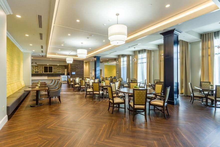 A modern restaurant interior featuring wooden floors, elegant lighting, and neatly arranged tables and chairs.
