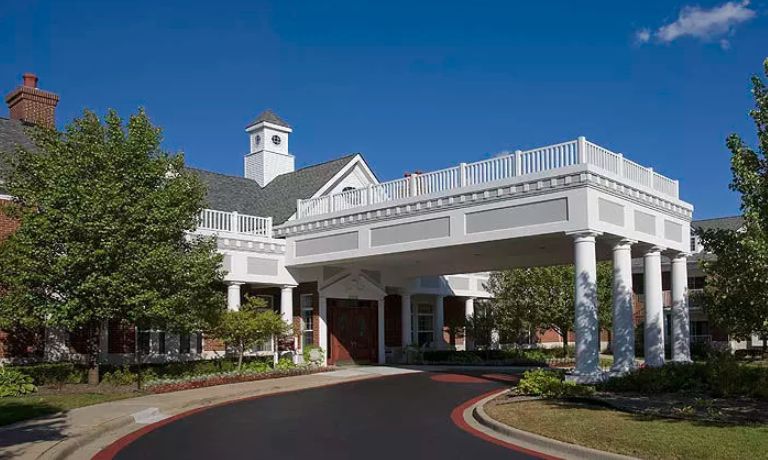 A large building with a covered entrance and columns, featuring a driveway.