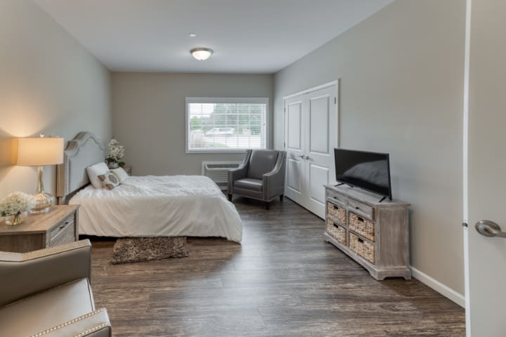 A modern and minimalist bedroom with neutral colors, featuring a bed, television, and chair.