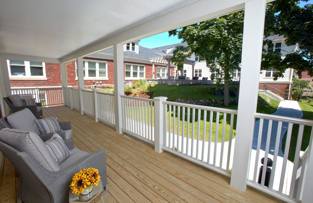 A cozy porch with white railings and outdoor seating overlooks a sunny garden area.