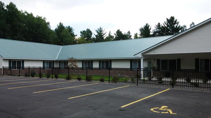 A single-story office building with a metal roof, surrounded by trees and a parking lot.