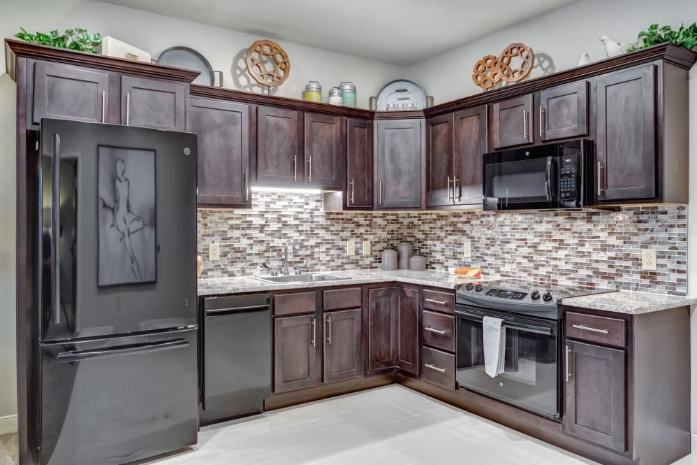 A modern kitchen with dark wood cabinets, stylish backsplash, and black appliances.