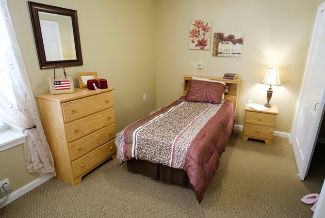 A cozy bedroom with a single bed, dresser, and warm lighting.