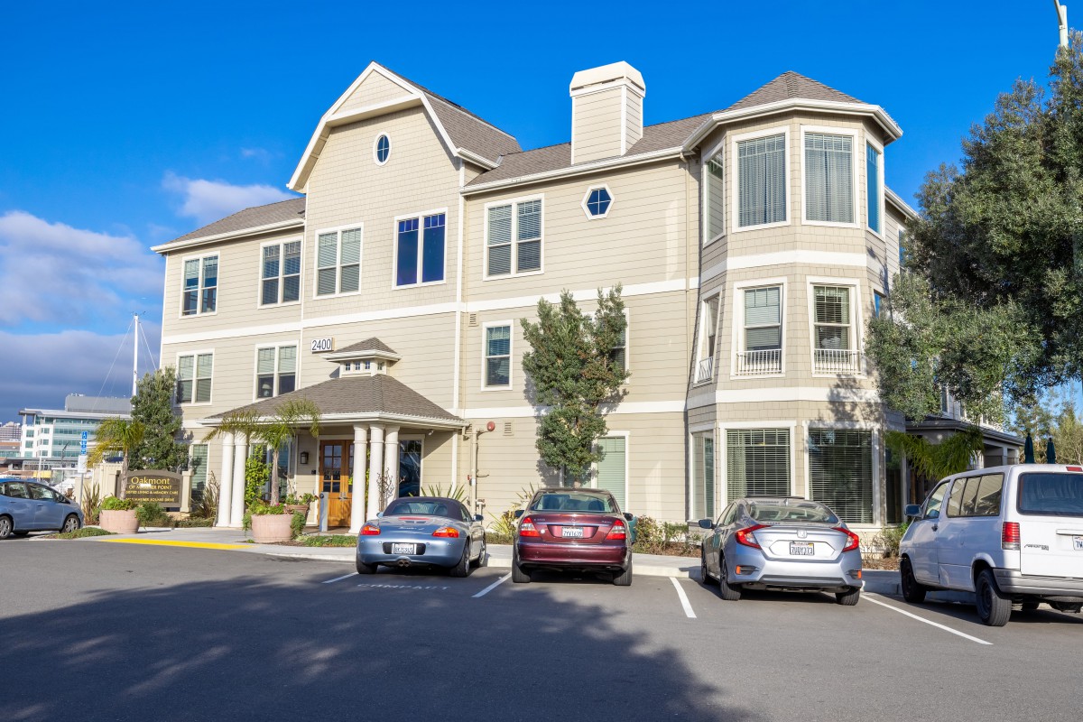 A multi-story residential building with parked cars in front during the daytime.