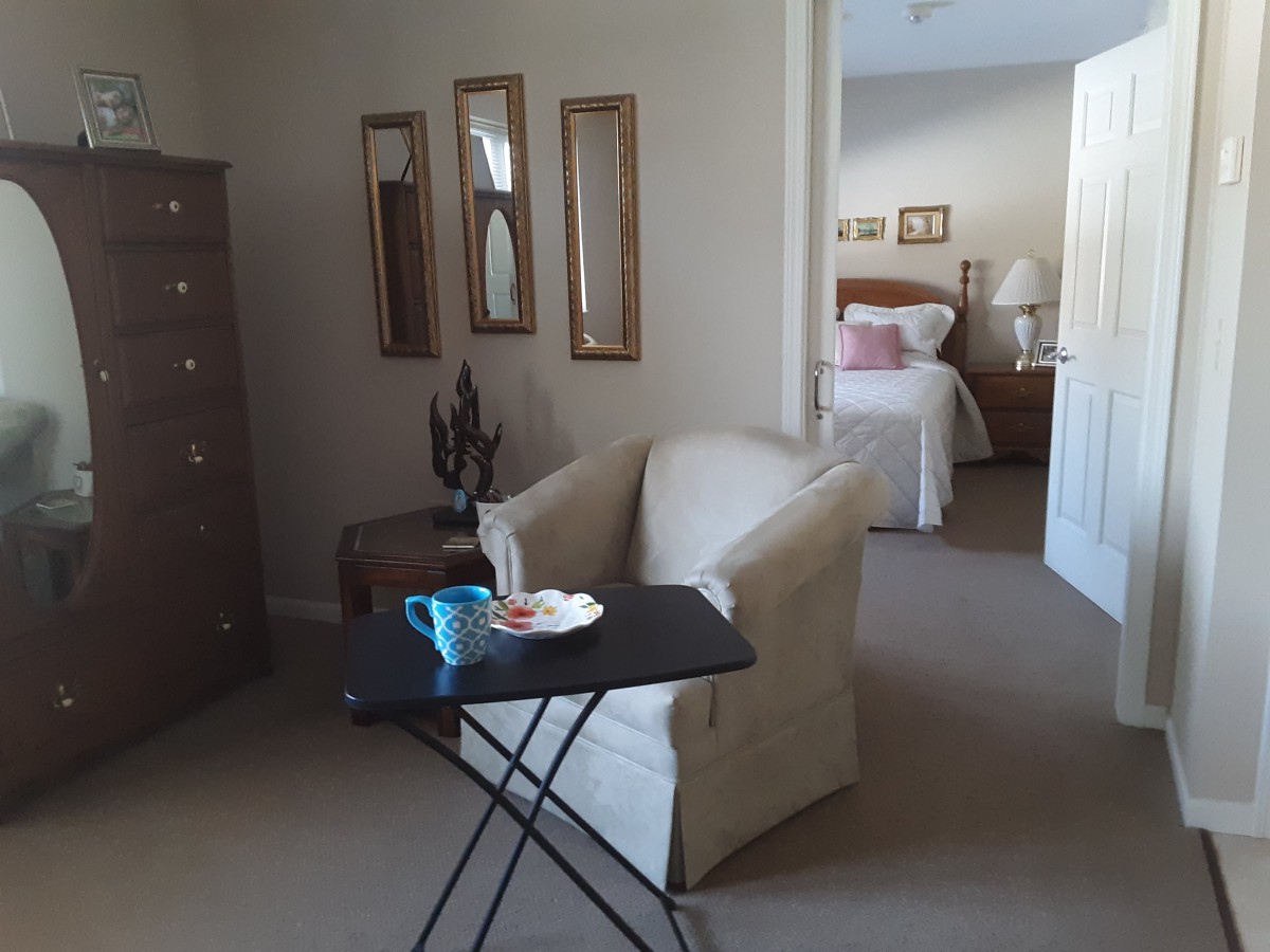 A cozy living space with a chair and table, leading to a bedroom in the background.