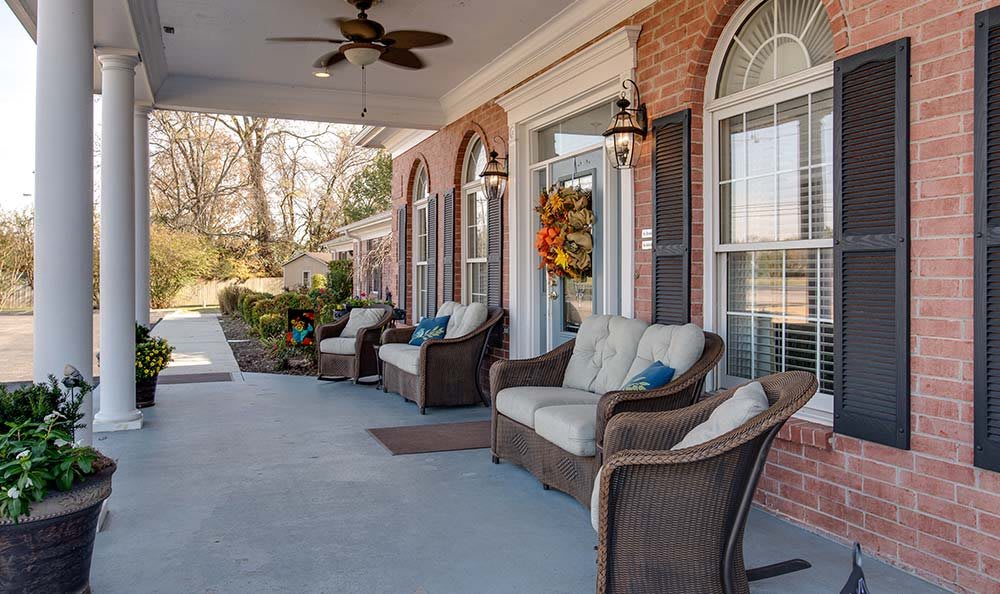 A cozy porch featuring wicker seating with cushions, adorned with fall decorations.