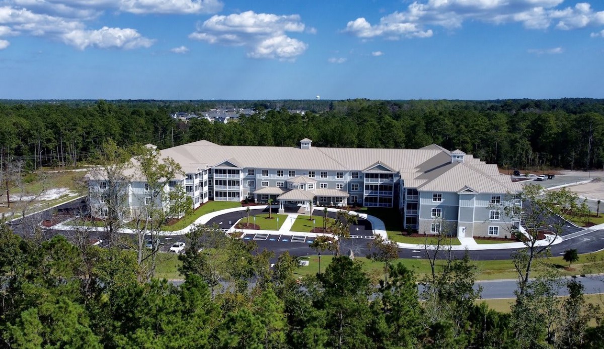 An aerial view of a large residential building surrounded by trees under a partly cloudy sky.